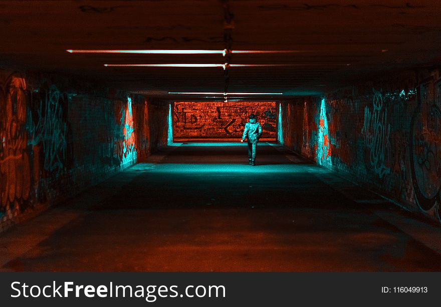 Person Wearing Jacket Walking on Tunnel With Red and Green Lights