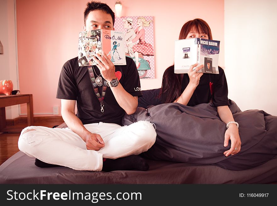 Couple Holding Books Sitting on Bed