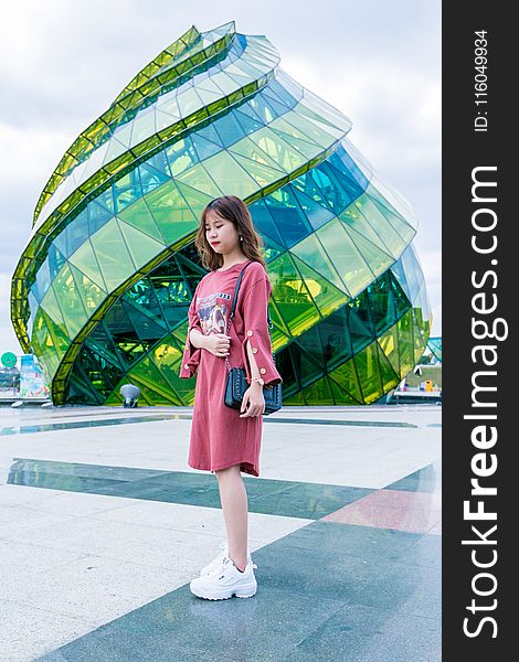 Girl Wearing Red Long-sleeved Dress and White Low-top Shoes Standing Near Green Glass Structure