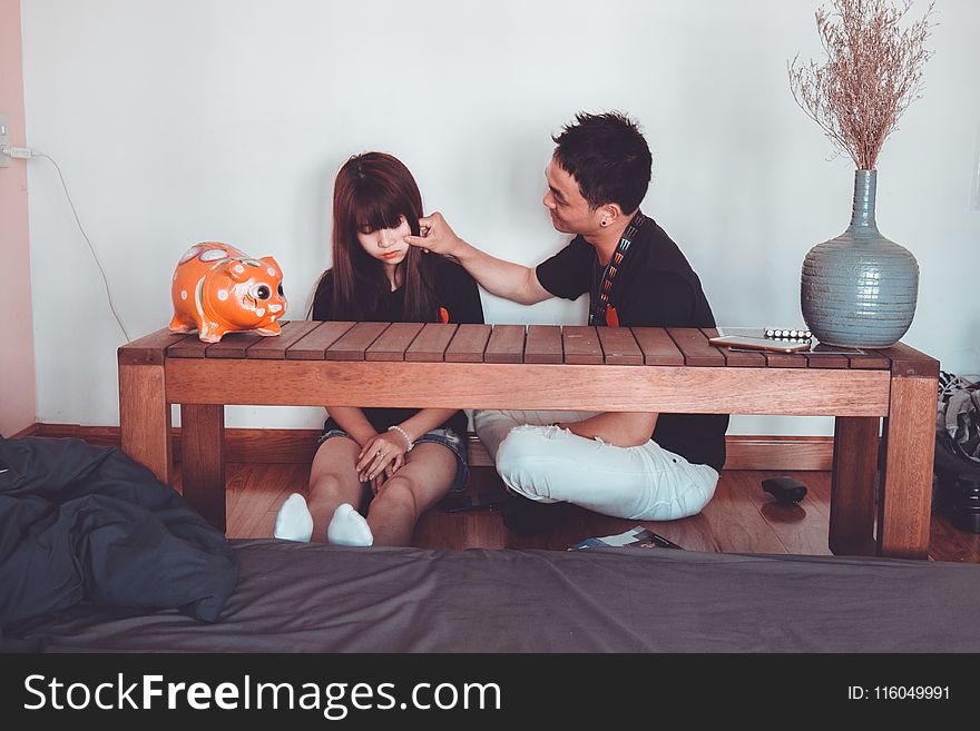 Man Pinching the Cheek of Woman Sitting Near Rectangular Brown Wooden Coffee Table