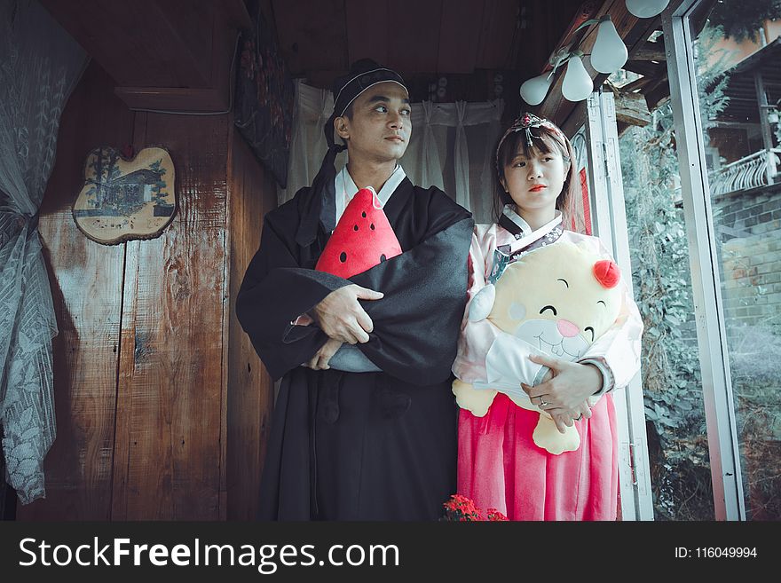 Man and Woman Holding Plush Toys Standing on Front of Brown Wall