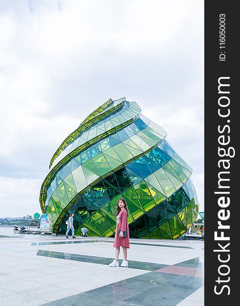 Woman In Red Dress Standing In Front Of Green Glass Elliptical Building