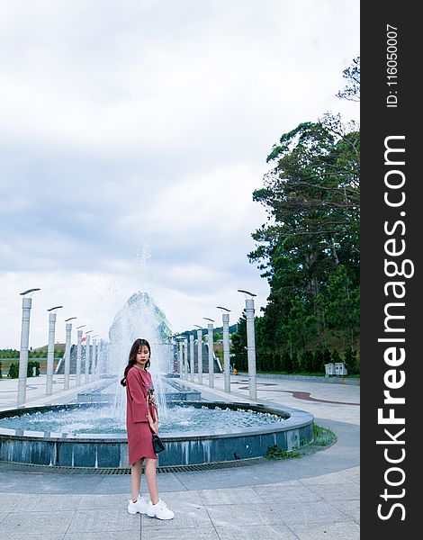 Woman in Red Long-sleeved Dress Standing Near Water Fountain at Daytime