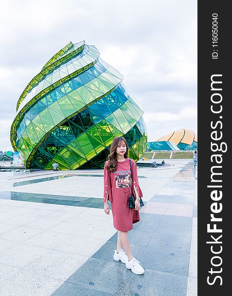 Woman in Red Long-sleeved Top Wearing White Sneakers Walking in Front of Green and Blue Glass Building