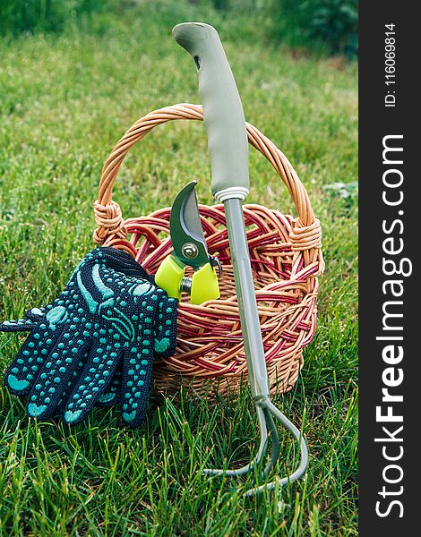 Small hand garden rake, pruner and gloves with wicker basket in green grass. Garden tools and equipment