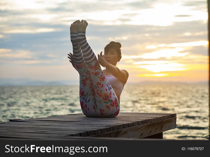 Woman pose yoga on wooden pier at sea side against beautiful sun