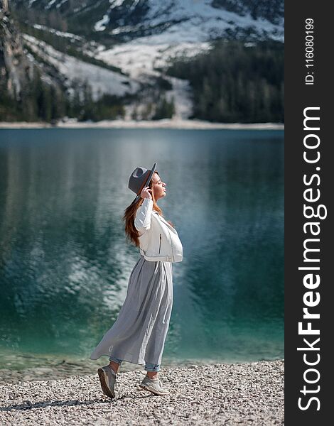 A girl in a hat and a long dress is walking along the lake. Lago di Bries in the north of Italy