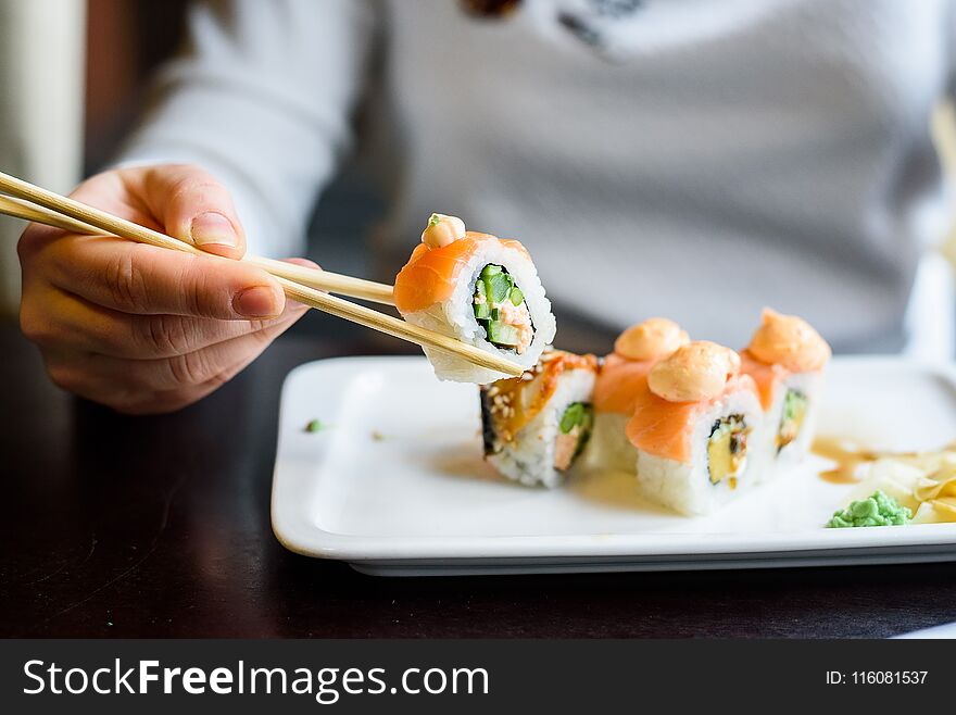 Young woman eats sushi rolls with chopsticks