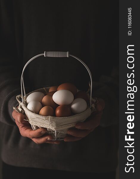 Man`s hands holding a basket with fresh brown and white chicken eggs over dark background