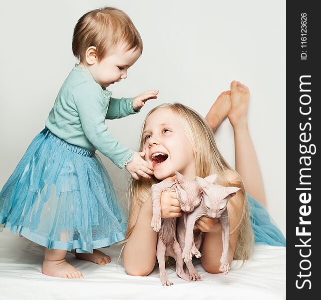 Cute baby and little girl playing with cats at home