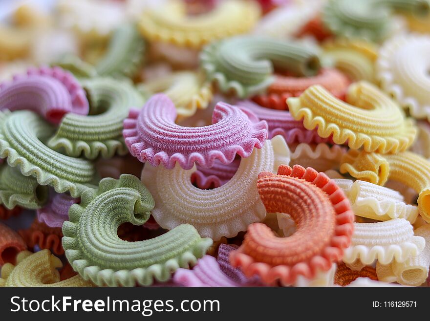 Background of colorful green, yellow, white, orange and pink italian crown pasta as creative food texture, close-up. Multicolor pasta texture pattern. Front focus