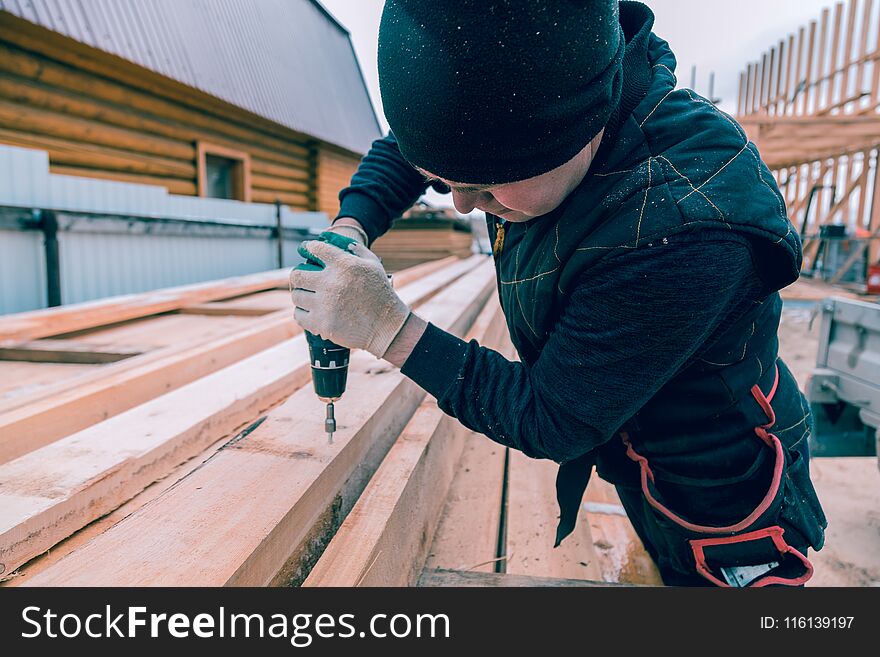 A man screws a screwdriver with an electric screwdriver into a wooden board. A man screws a screwdriver with an electric screwdriver into a wooden board