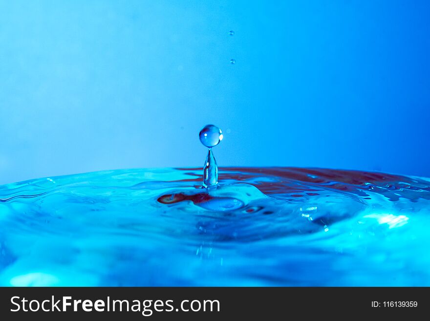 Drop of water falling in blue water and blue background.
