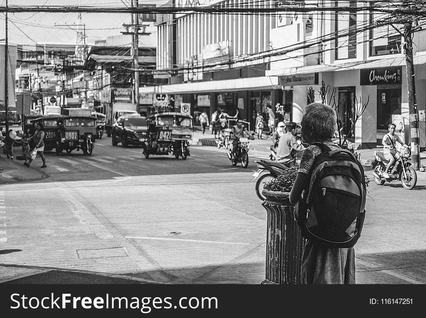 Person Wearing a Backpack in the Middle of the Street in Grayscale Photo