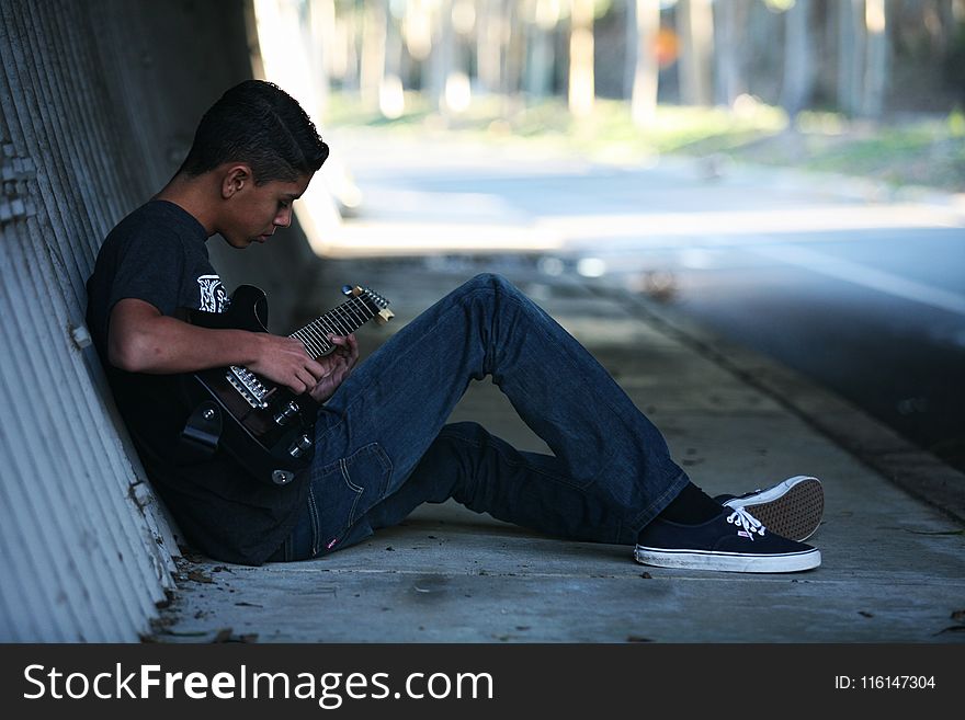 Man Sitting Near Wall Playing Guitar