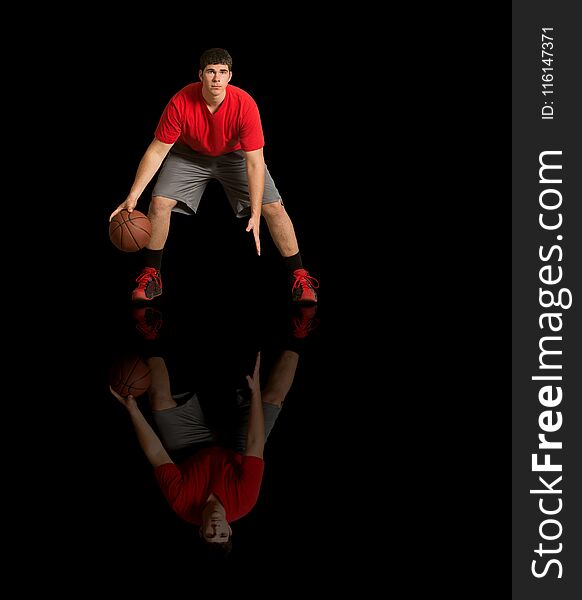 Young athlete in red tee shirt playing basketball on reflective, black surface. Young athlete in red tee shirt playing basketball on reflective, black surface