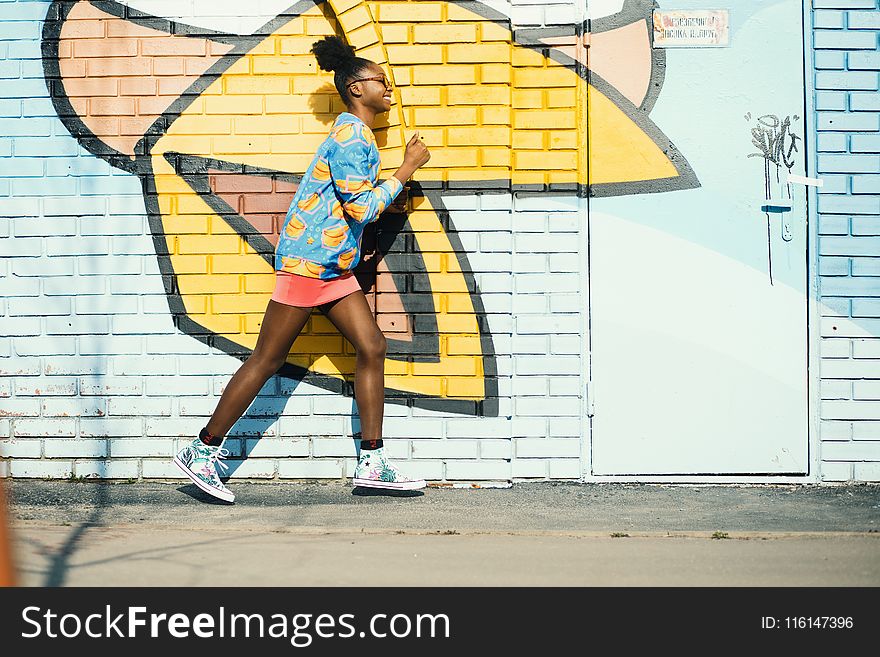 Woman Wearing Blue And Yellow Long-sleeved Shirt Walking Near White And Yellow Painted Wall