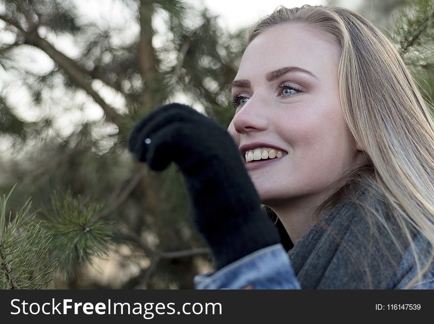 Woman Wearing Grey Scarf Holding a Pine Leaf While Smiling