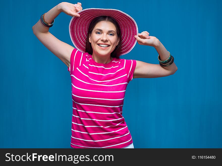 Smiling young woman wearing pink beach hat posing against blue background.