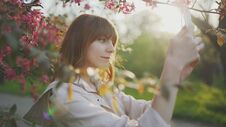 Young Attractive Red-haired Woman Taking Photos Of Spring Flowers Of Cherry Or Sakura Blossoms On Smartphone At Sunset In Park Royalty Free Stock Photo