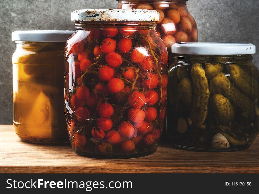 Homemade preserving, canning food, pickled or fermented vegetables in glass jars over kitchen drawer, grey stone wall background, copy space