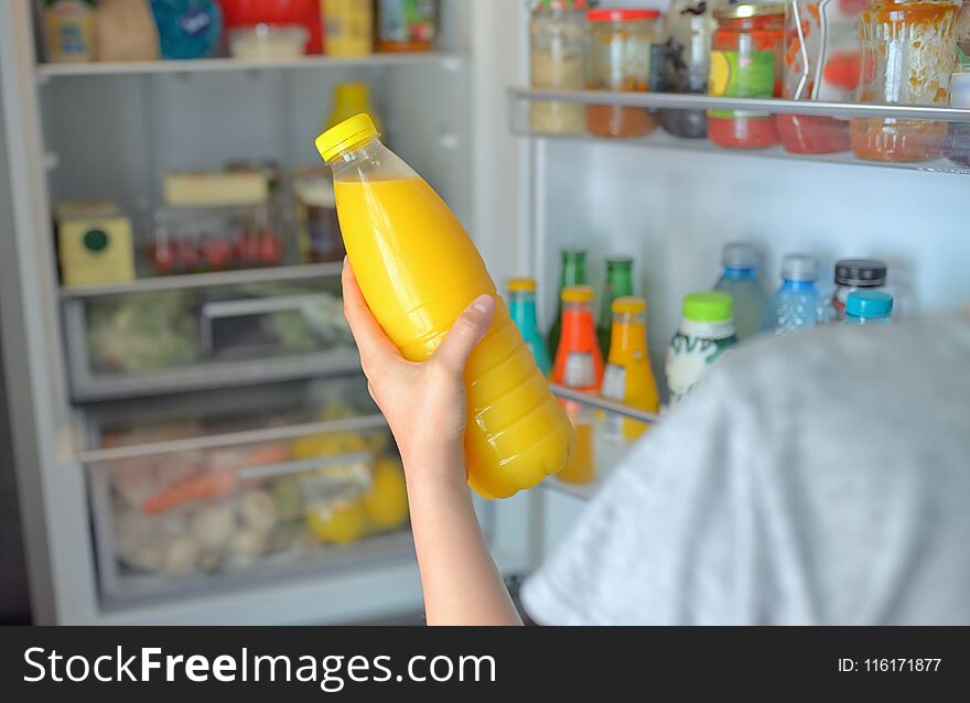 Teenage girl takes the orange juice from the open refrigerator