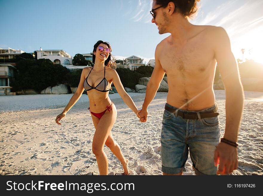 Happy couple in love on beach summer vacation. Joyful men and women walking along the beach holding hands.