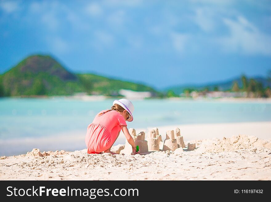 Little adorable girl at tropical beach making sand castle