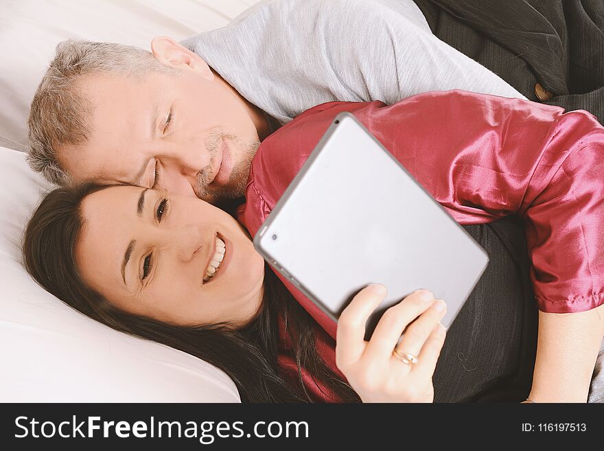 Happy middle-aged couple watching video on tablet at home. Indoors