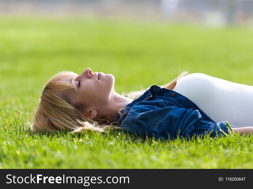 Pretty young woman relaxing while lying on the grass in the park.