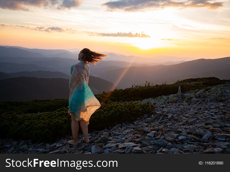 Romantic woman in a scarf stands on the top during sunset