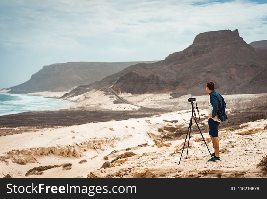 Photographer With Camera In Desert Admitting Unique Landscape Of Sand Dunes Volcanic Cliffs On The Atlantic Coast. Baia