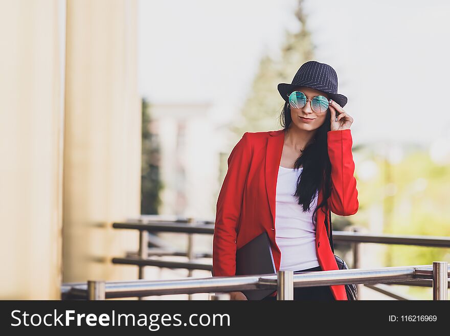 Portret of Happy hipster young woman with laptop wearing sunglasses, black hat and red jacket. Student girl with laptop