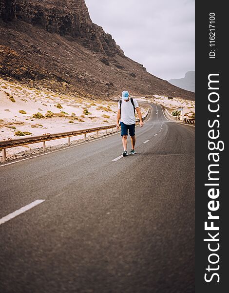 Traveler with backpack standing in the center of an epic winding road. Huge volcanic mountains in the distance behind