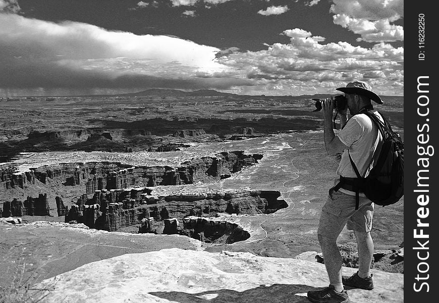 Grayscale Photo of Man Taking Photo of Canyons