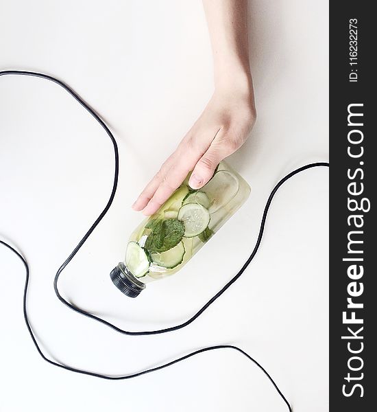 Person Holding Bottle and Cucumber
