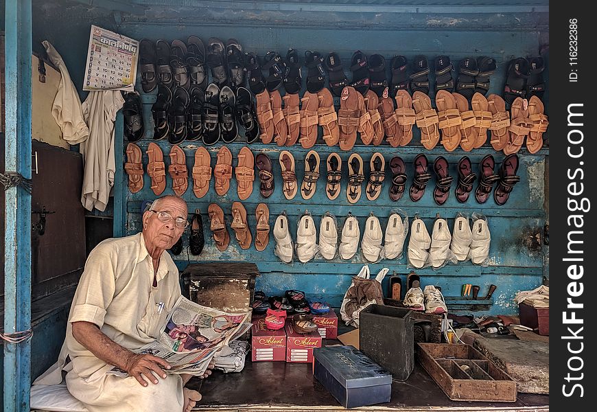 Man Reading Newspaper Surrounded by Shoes