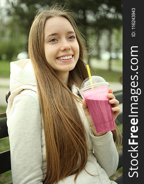 A girl is sitting with a pink smoothie on a bench. Concept detox. A girl is sitting with a pink smoothie on a bench. Concept detox.