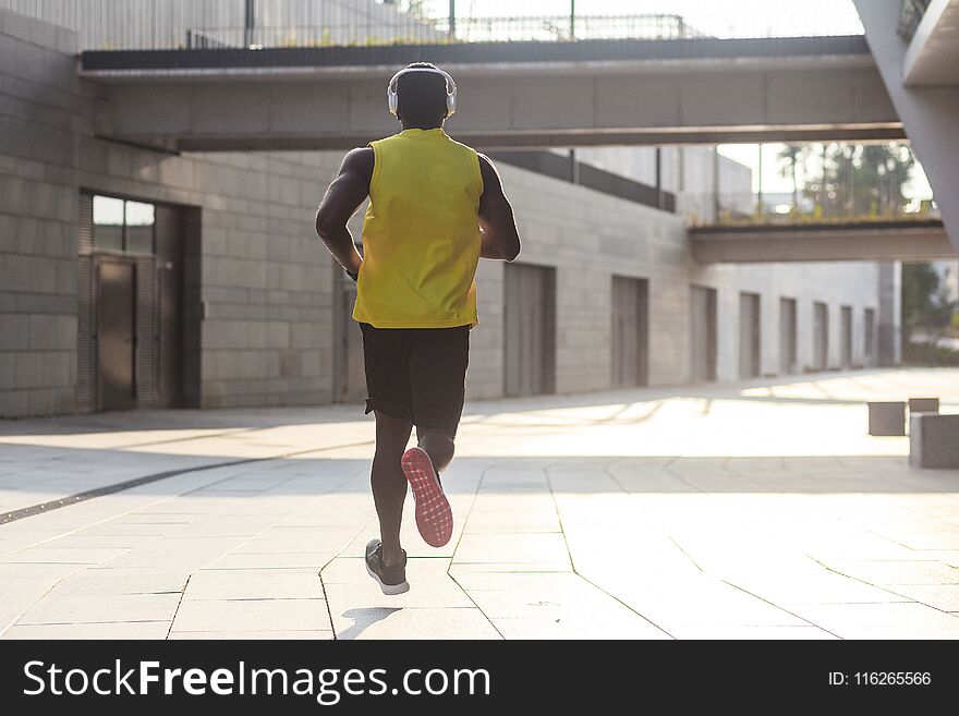 Young fit man in yellow t-shirt running sunset outdoors, autumn running, attractive dark skinned runner jogging fast in the park with beautiful light on background, sport concept. Young fit man in yellow t-shirt running sunset outdoors, autumn running, attractive dark skinned runner jogging fast in the park with beautiful light on background, sport concept