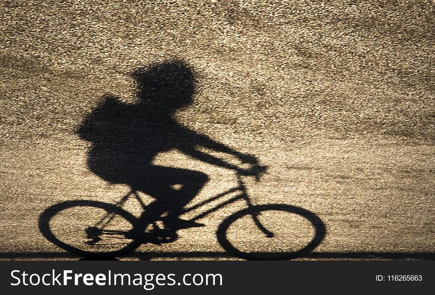 Defocused blurry shadow silhouette of a young person riding a bi