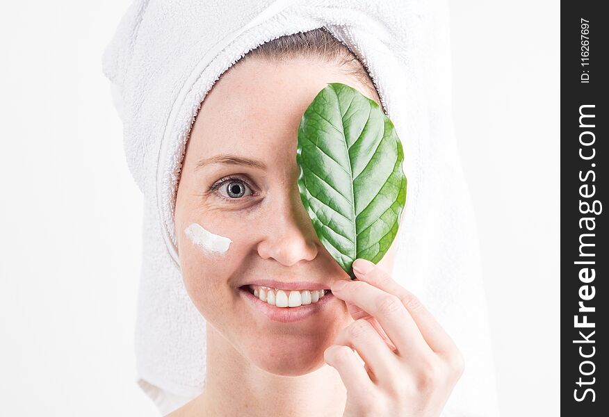 Natural Cosmetics: a girl with a white towel on her head smiles and covers one eye with a green leaf.