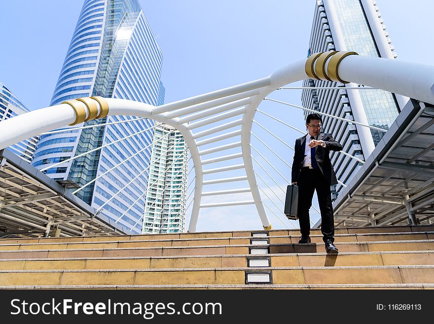 The asian businessman has holding a black bag and looking on watch in hurrying time.