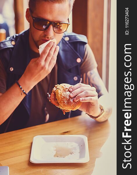 Attractive hipster dressed in leather jacket eating a vegan burger. Attractive hipster dressed in leather jacket eating a vegan burger.