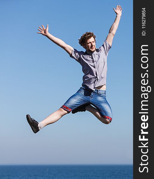 Carefree man jumping by sea ocean. Happy guy having fun. Summer happiness and freedom.