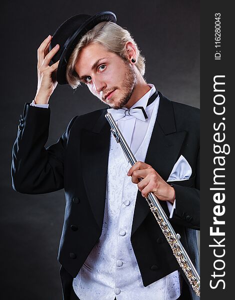 Classical music, passion and hobby concept. Elegantly dressed musician man holding flute wearing black hat. Studio shot on dark background. Classical music, passion and hobby concept. Elegantly dressed musician man holding flute wearing black hat. Studio shot on dark background