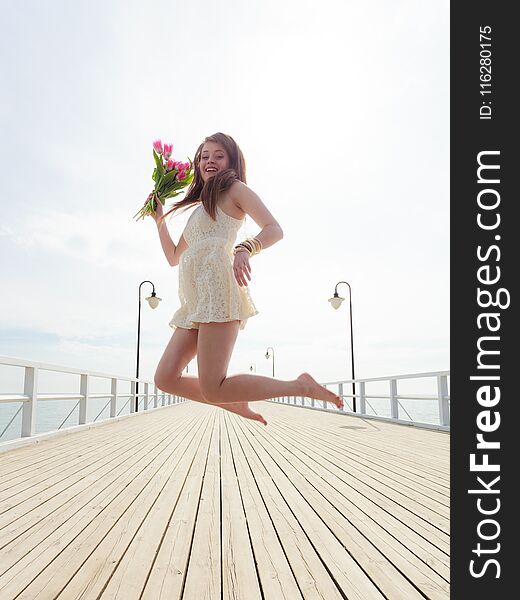 Woman Jumping On Pier With Flowers In Hand