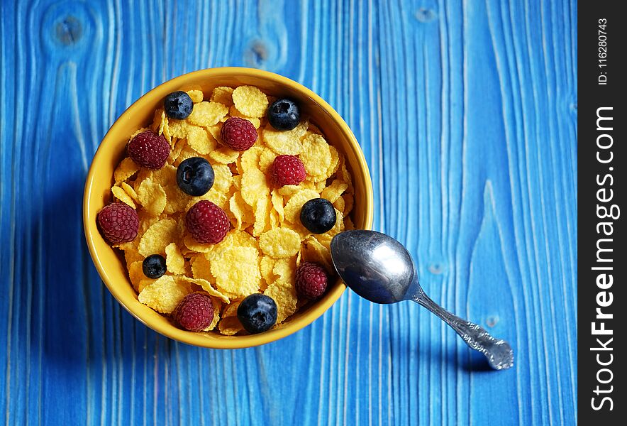 Cornflakes with berries raspberries and blueberries on blue wooden background. Close up.