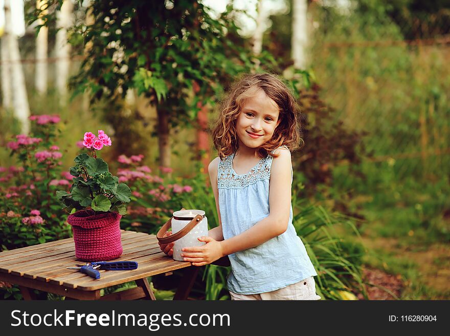 Happy child girl decorating evening summer garden with candle holder. Smiling kid helps on backyard on vacations