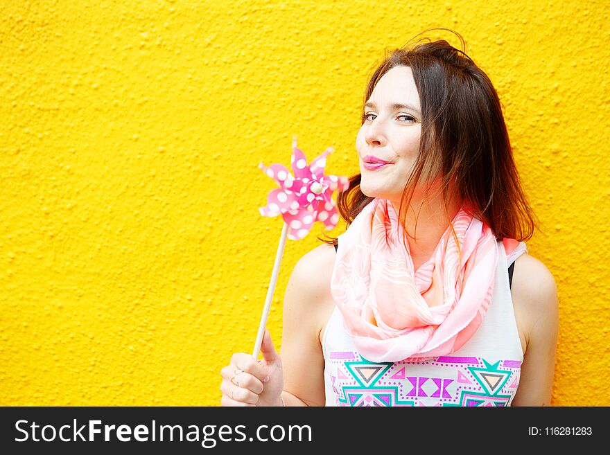 Young brunette woman standing at yellow wall with pinwheel. Young brunette woman standing at yellow wall with pinwheel