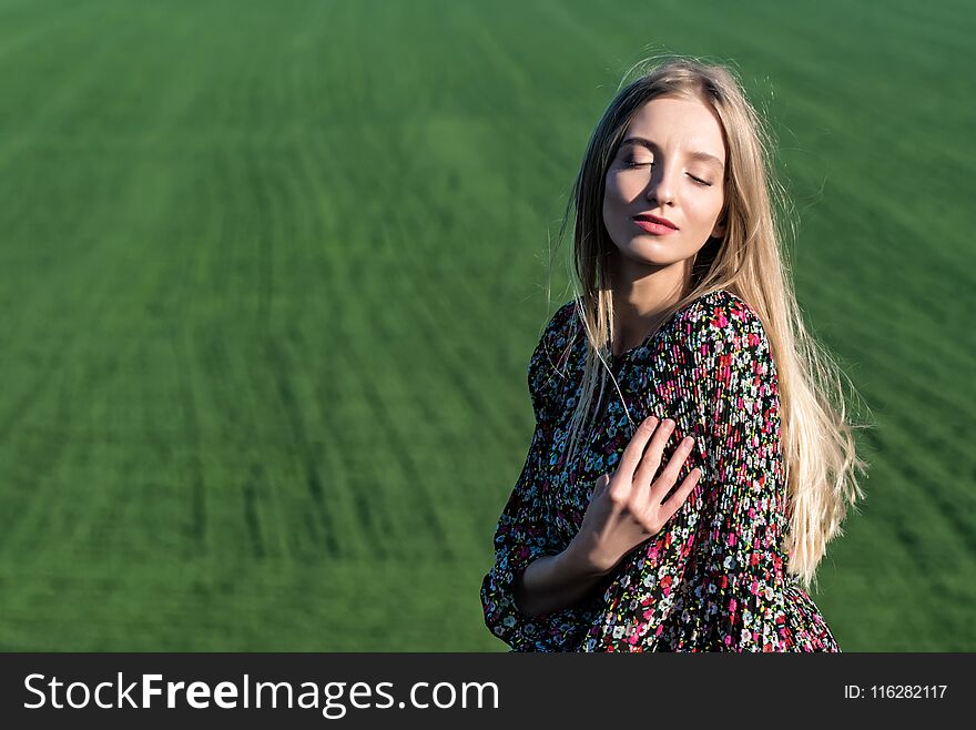 Romantic picture of young pretty model in dress standing on rock with beautiful green field in background. Romantic picture of young pretty model in dress standing on rock with beautiful green field in background